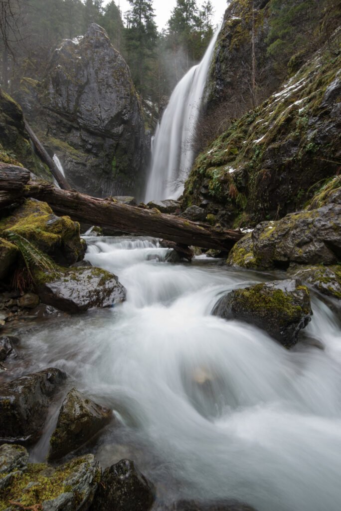 A large waterfall thundering over rocks and logs